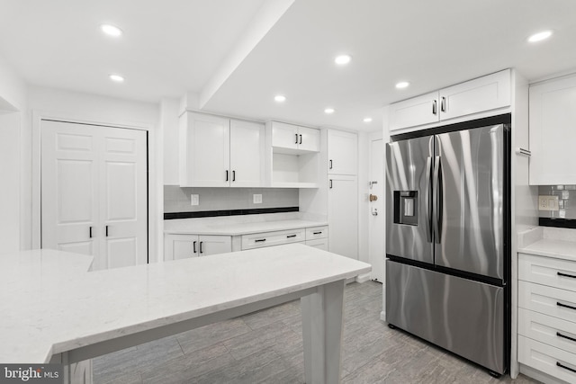 kitchen with light stone counters, white cabinetry, backsplash, light wood-type flooring, and stainless steel refrigerator with ice dispenser