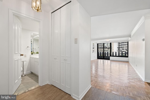 hallway with a notable chandelier, crown molding, and light parquet floors