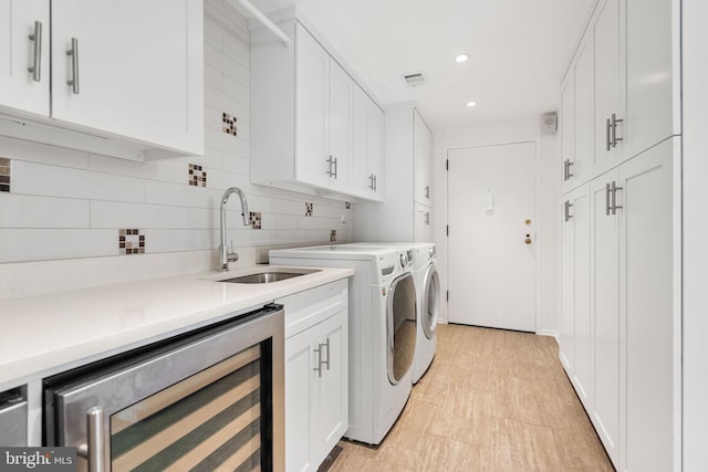 clothes washing area featuring wine cooler, sink, cabinets, and washing machine and clothes dryer