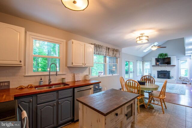 kitchen with backsplash, a brick fireplace, stainless steel dishwasher, vaulted ceiling, and a healthy amount of sunlight