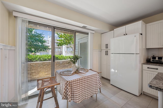 kitchen with white fridge, light tile patterned flooring, white cabinetry, and dark stone counters