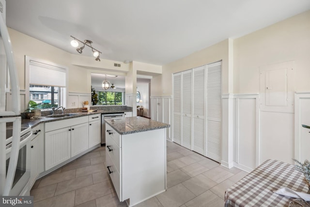 kitchen featuring white range with electric cooktop, stainless steel dishwasher, white cabinetry, a kitchen island, and a sink