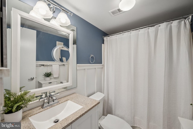 full bathroom featuring toilet, a decorative wall, a wainscoted wall, vanity, and visible vents