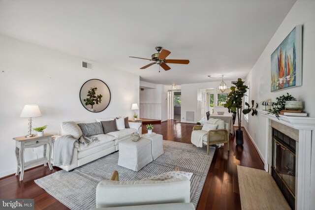 living area with baseboards, visible vents, dark wood-type flooring, a fireplace, and ceiling fan with notable chandelier