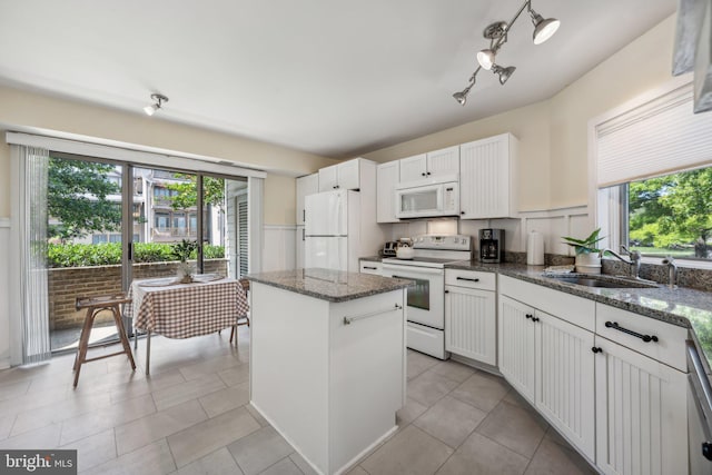 kitchen featuring dark stone counters, sink, a center island, white cabinets, and white appliances