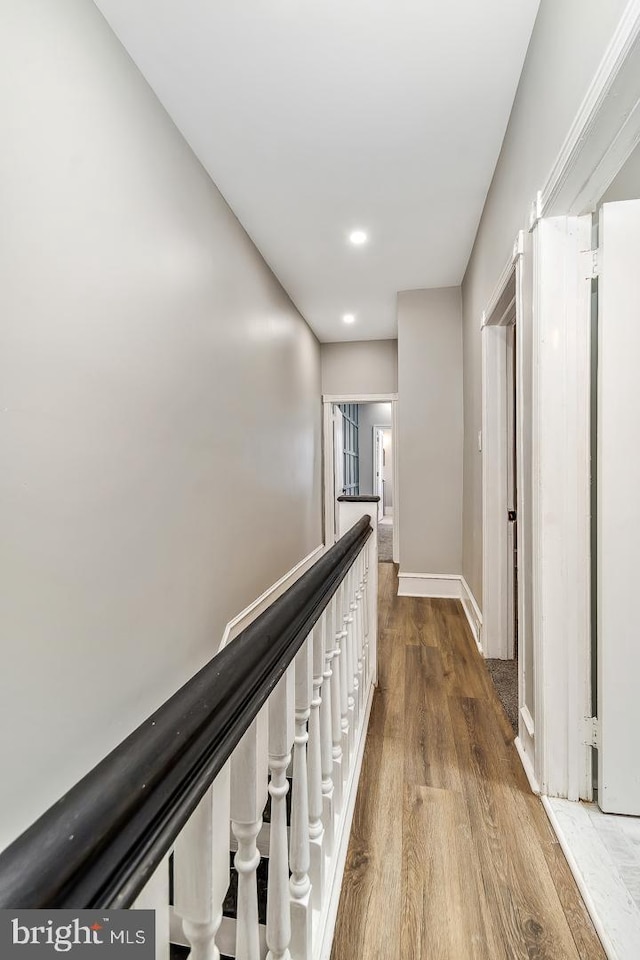 corridor featuring baseboards, wood finished floors, and an upstairs landing