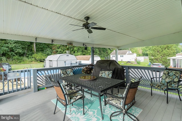 wooden deck with ceiling fan, a storage unit, outdoor dining area, and an outbuilding