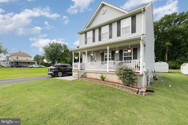 view of front facade featuring covered porch, a storage shed, aphalt driveway, and a front yard