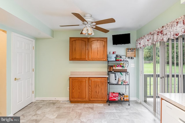 interior space featuring brown cabinets, baseboards, light countertops, and a ceiling fan