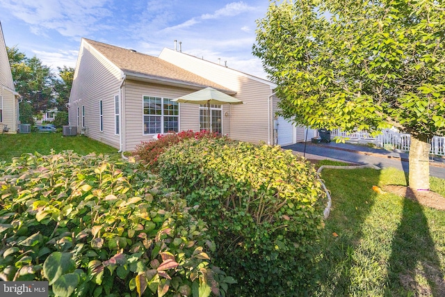 rear view of house featuring a garage, a lawn, and central air condition unit