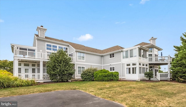 rear view of property featuring a balcony and a yard