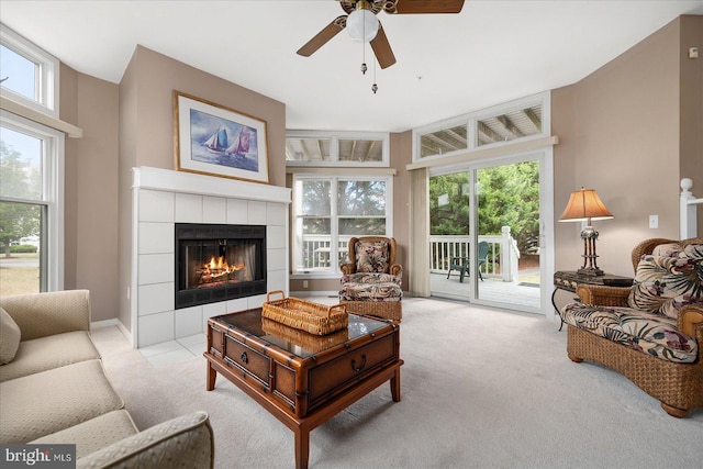 carpeted living room with ceiling fan, a tile fireplace, a high ceiling, and a healthy amount of sunlight