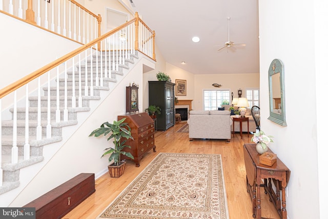 living room with stairs, high vaulted ceiling, a fireplace, and wood finished floors