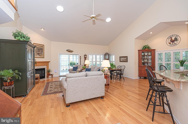 living area with high vaulted ceiling, a tile fireplace, recessed lighting, baseboards, and light wood-style floors