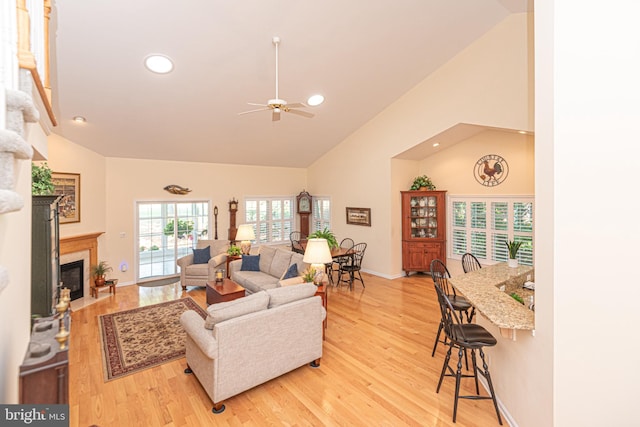 living area with baseboards, a fireplace with flush hearth, high vaulted ceiling, and wood finished floors