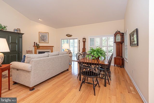 dining area with light wood-style floors, vaulted ceiling, a fireplace, and baseboards