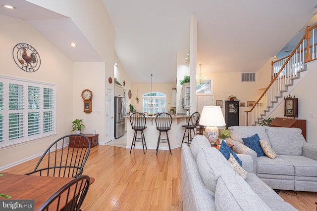 living room featuring visible vents, light wood-style floors, a chandelier, baseboards, and stairs