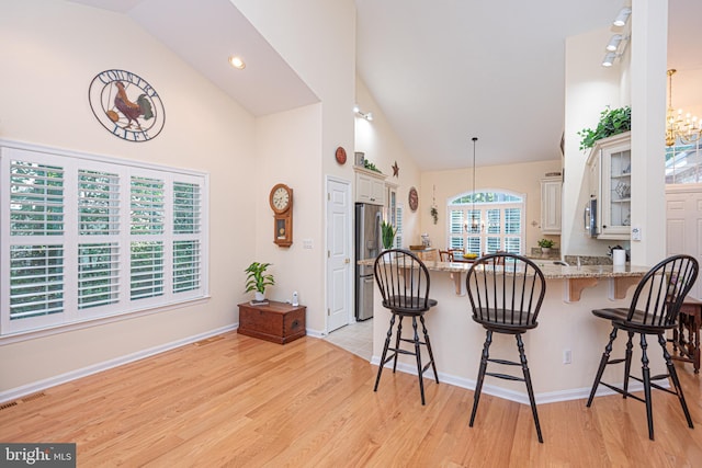 kitchen featuring visible vents, light stone counters, a kitchen breakfast bar, a peninsula, and an inviting chandelier