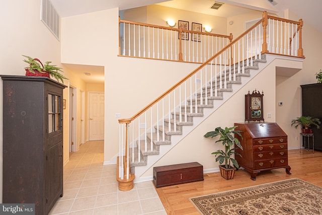 staircase featuring wood finished floors, a towering ceiling, visible vents, and baseboards