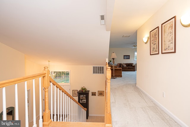 corridor with baseboards, an upstairs landing, visible vents, and light colored carpet