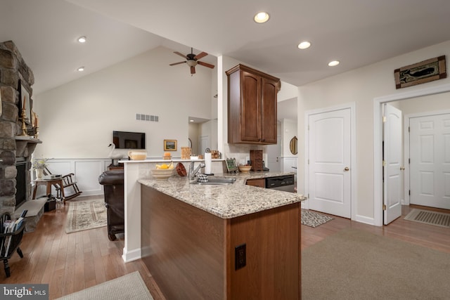 kitchen featuring light stone counters, light wood-type flooring, kitchen peninsula, ceiling fan, and a stone fireplace