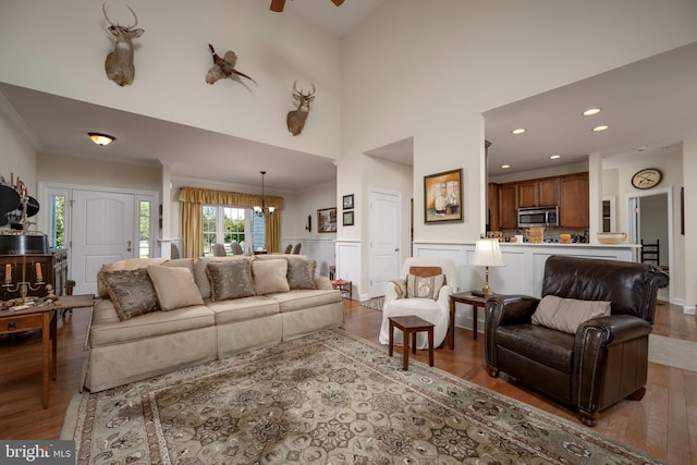 living room featuring ceiling fan, a towering ceiling, light hardwood / wood-style flooring, and ornamental molding