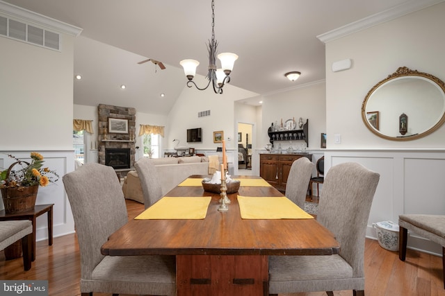 dining space with ornamental molding, vaulted ceiling, a fireplace, a notable chandelier, and hardwood / wood-style flooring