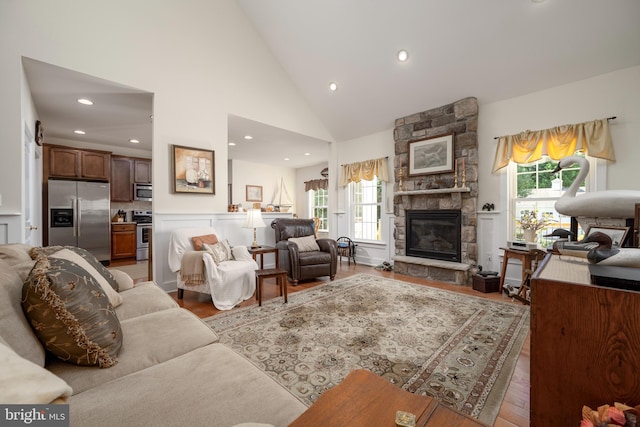 living area with light wood finished floors, recessed lighting, high vaulted ceiling, and a stone fireplace