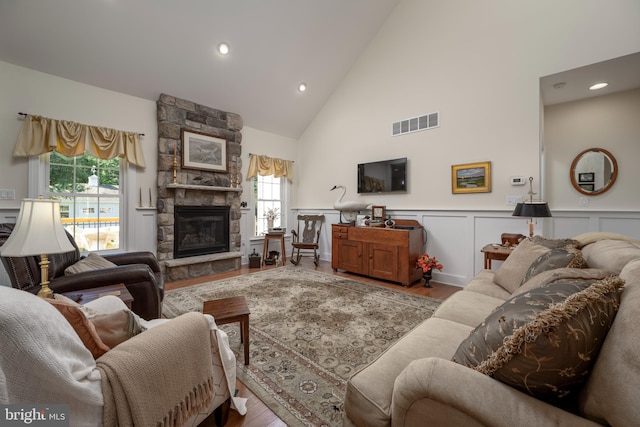 living room with high vaulted ceiling, a stone fireplace, and light hardwood / wood-style flooring