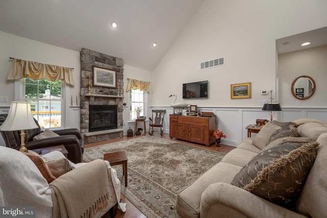 living area with a stone fireplace, light wood-style flooring, wainscoting, and visible vents