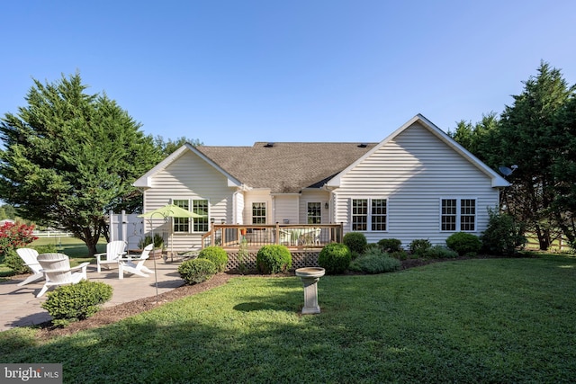 rear view of house with a shingled roof, a deck, a lawn, and a patio