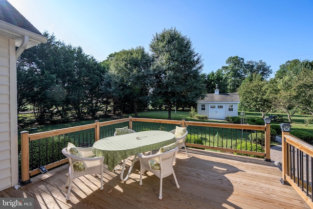 wooden terrace featuring outdoor dining space, a lawn, and an outdoor structure