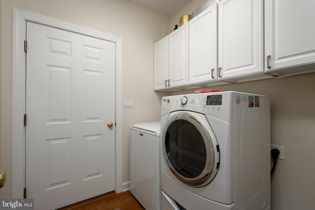 clothes washing area with hardwood / wood-style floors, washer and dryer, and cabinets