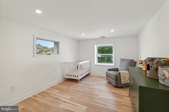 bedroom with light wood-type flooring and a nursery area