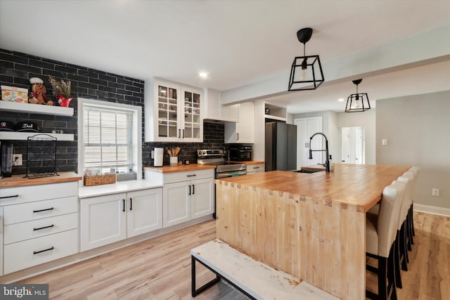 kitchen with white cabinetry, sink, stainless steel electric range, a kitchen island with sink, and wooden counters