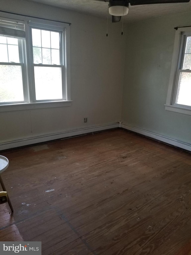 unfurnished room with a baseboard heating unit, dark wood-type flooring, ceiling fan, and a wealth of natural light