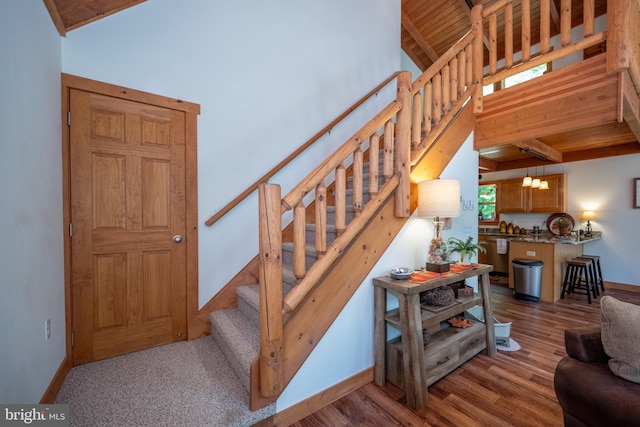 stairway featuring wooden ceiling, high vaulted ceiling, baseboards, and wood finished floors