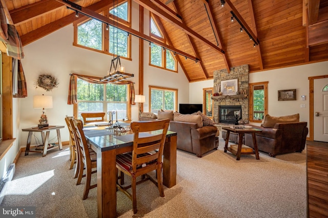 dining room featuring wood ceiling, carpet flooring, a stone fireplace, and beam ceiling