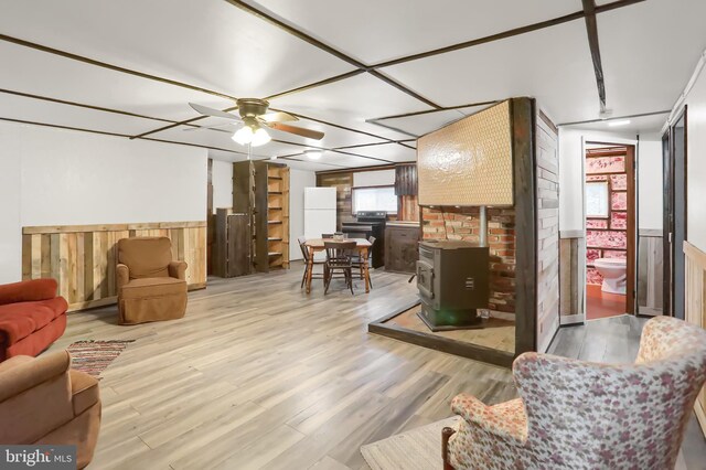 living room with light hardwood / wood-style flooring, ceiling fan, and a wood stove