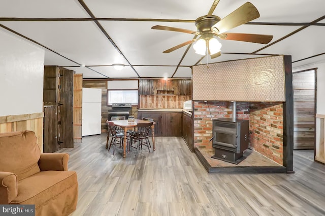 dining space featuring wooden walls, ceiling fan, hardwood / wood-style floors, and a wood stove