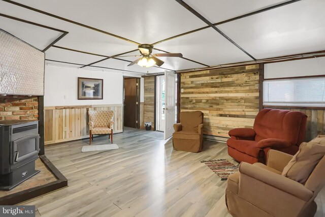 living room with light wood-type flooring, a wood stove, wooden walls, and ceiling fan