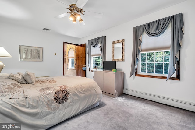 carpeted bedroom with a baseboard heating unit, multiple windows, and ceiling fan