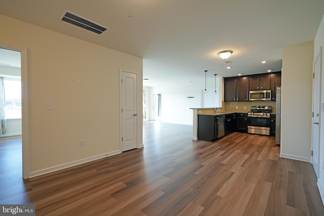 kitchen with kitchen peninsula, appliances with stainless steel finishes, hardwood / wood-style floors, and dark brown cabinets