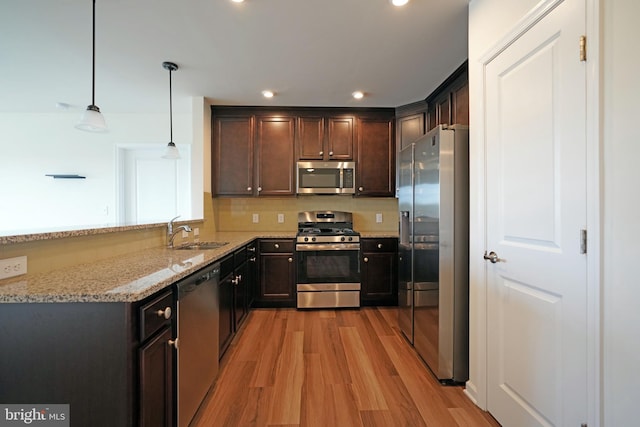 kitchen featuring light wood-type flooring, pendant lighting, light stone counters, sink, and stainless steel appliances