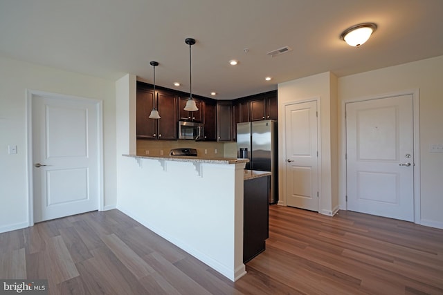 kitchen featuring wood-type flooring, appliances with stainless steel finishes, light stone countertops, decorative light fixtures, and kitchen peninsula