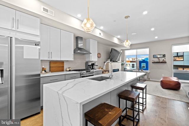 kitchen with white cabinets, sink, high end appliances, wall chimney exhaust hood, and light hardwood / wood-style flooring