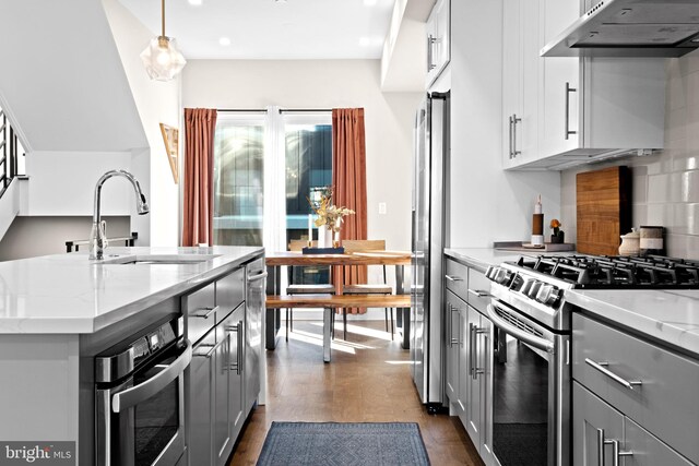 kitchen with gray cabinets, pendant lighting, dark wood-type flooring, light stone countertops, and appliances with stainless steel finishes