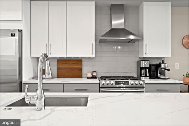 kitchen with wall chimney range hood, sink, stainless steel appliances, light stone countertops, and white cabinets