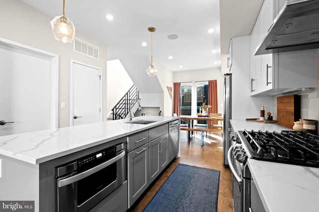 kitchen featuring dark wood-type flooring, decorative light fixtures, an island with sink, appliances with stainless steel finishes, and exhaust hood