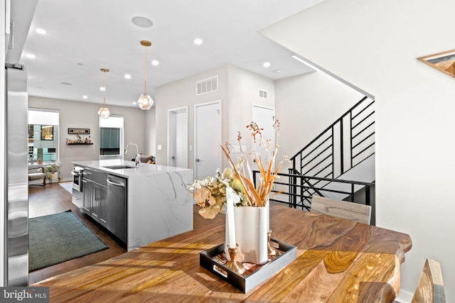 kitchen featuring pendant lighting, dark hardwood / wood-style flooring, a center island with sink, sink, and appliances with stainless steel finishes